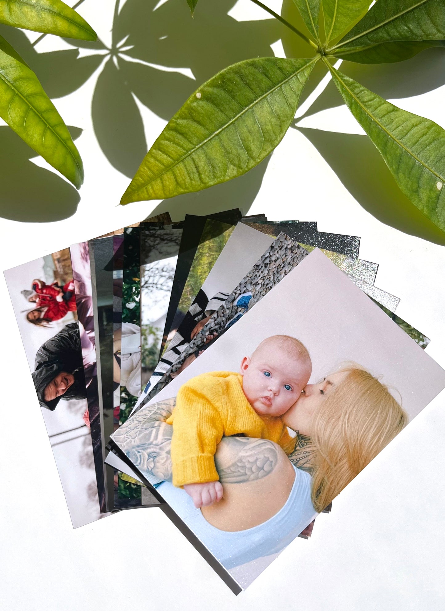 A small collection of photo prints fanned out to showcase the luster photo paper printed through Fotobox. The featured photo shows a baby wearing a yellow knit sweater with their mother kissing the baby on the cheek.